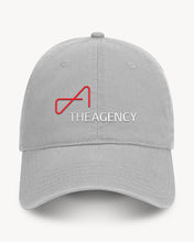 Load image into Gallery viewer, A gray baseball cap with a velcro back closure, featuring a red and white logo that reads 'THE AGENCY'.